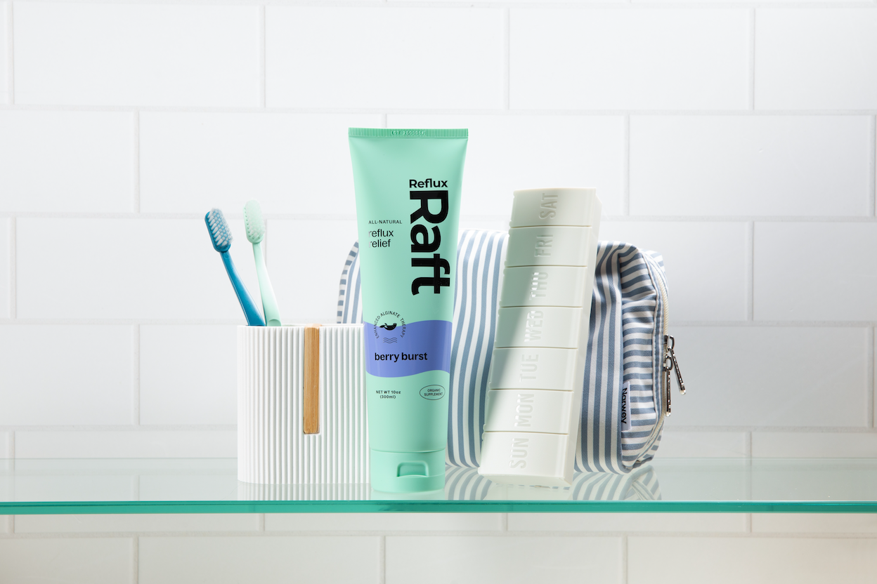 RefluxRaft Berry Burst alginate supplement tube displayed on a bathroom shelf with toothbrushes and a weekly pill organizer