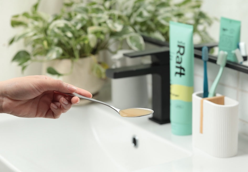 Hand holding a spoonful of RefluxRaft Lemon Ginger alginate gel in a bathroom setting